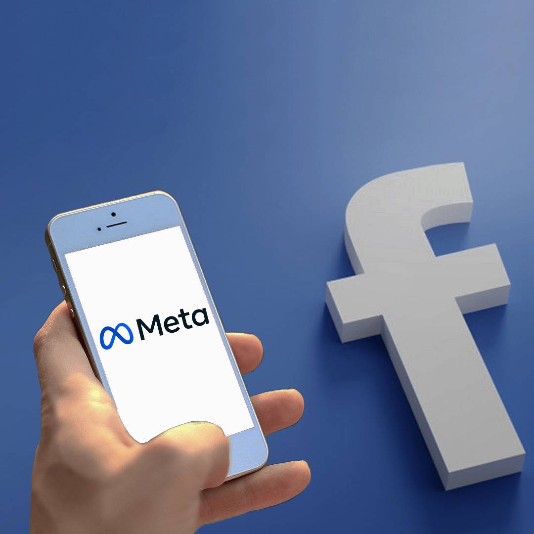 A phone showing Meta logo in front of a wall with the Facebook logo.