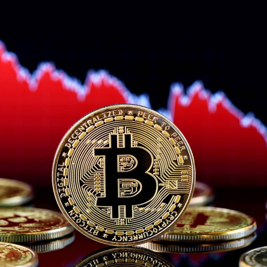 A Bitcoin physical coin in front of a dropping chart.